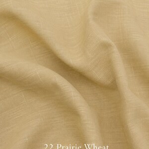 Op de afbeelding: Een lichtbruine, beige tencel-linnen stof met een zichtbare geweven textuur en zachte plooien. De tekst 22 Prairie Wheat en 180G TENCEL-LINEN FABRIC is in het wit onderaan in het midden van de afbeelding op de stof gedrukt.