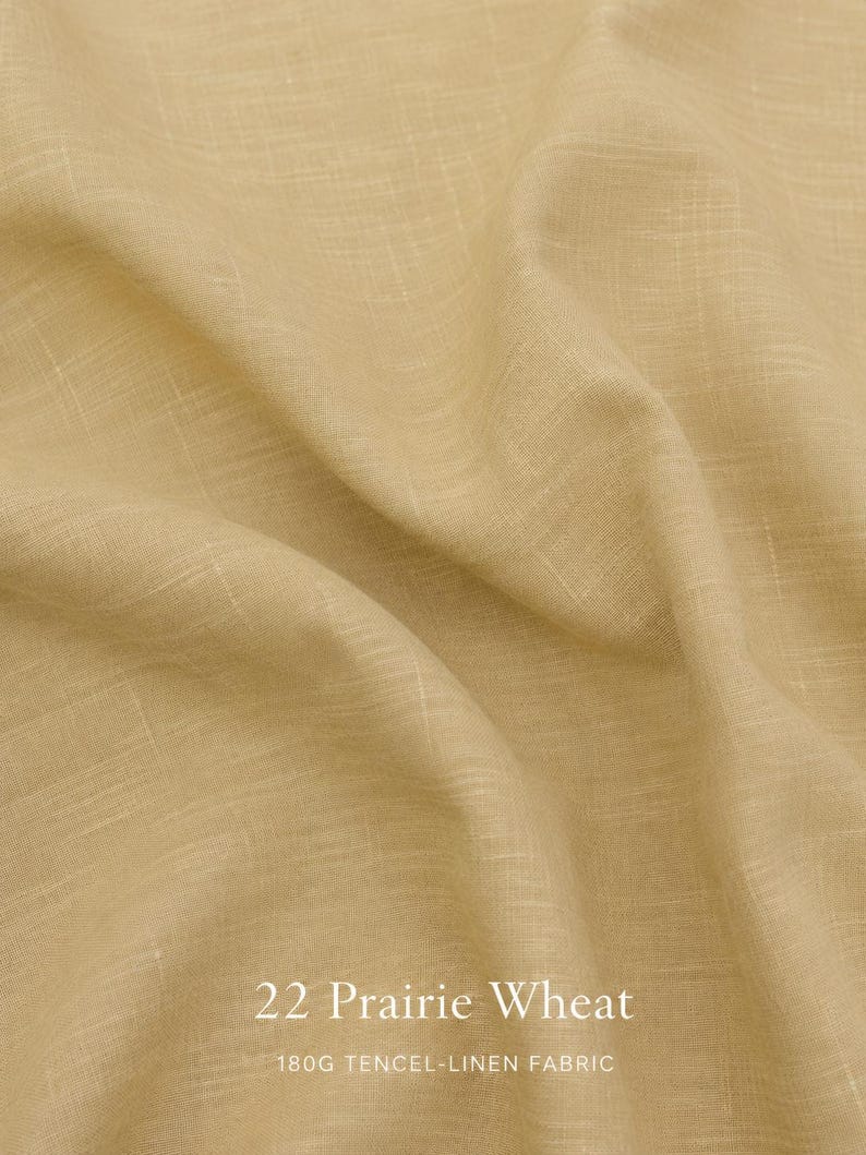 Op de afbeelding: Een lichtbruine, beige tencel-linnen stof met een zichtbare geweven textuur en zachte plooien. De tekst 22 Prairie Wheat en 180G TENCEL-LINEN FABRIC is in het wit onderaan in het midden van de afbeelding op de stof gedrukt.