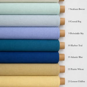 Op de afbeelding: Negen horizontale rollen stof verticaal gestapeld, elk met een kartonnen kern. De kleuren zijn Alpine Snow, Seafoam Breeze, Coastal Fog, Periwinkle Sky, Harbor Teal, Atlantic Blue, Prairie Wheat, Lemon Chiffon en Canyon Oak.