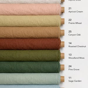 Op de afbeelding: Negen horizontale rollen textiel met een textuur in diverse kleuren, gelabeld met nummers en namen: 01 Alpine Snow, 21 Apricot Cream, 22 Prairie Wheat, 25 Canyon Oak, 14 Roasted Chestnut, 13 Woodland Moss, 24 Pine Grove, 11 Sage Garden en 08 Coastal Fog.