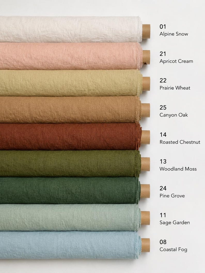 Op de afbeelding: Negen horizontale rollen textiel met een textuur in diverse kleuren, gelabeld met nummers en namen: 01 Alpine Snow, 21 Apricot Cream, 22 Prairie Wheat, 25 Canyon Oak, 14 Roasted Chestnut, 13 Woodland Moss, 24 Pine Grove, 11 Sage Garden en 08 Coastal Fog.