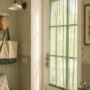 May include: A sheer sage green curtain panel hangs over a glass-paned door. The fabric is lightweight and semi-transparent, featuring a gathered top and bottom rod pocket design that covers the rectangular window section of the white door frame.