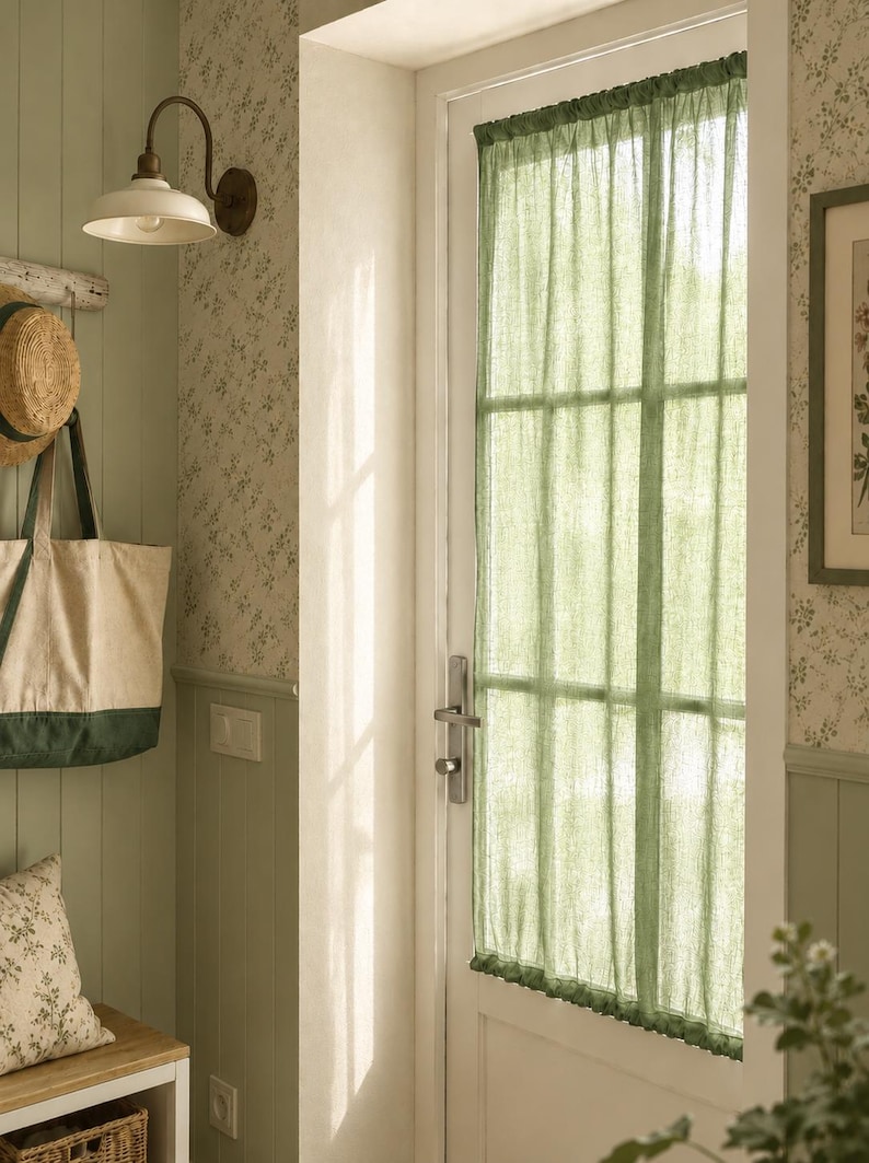 May include: A sheer sage green curtain panel hangs over a glass-paned door. The fabric is lightweight and semi-transparent, featuring a gathered top and bottom rod pocket design that covers the rectangular window section of the white door frame.