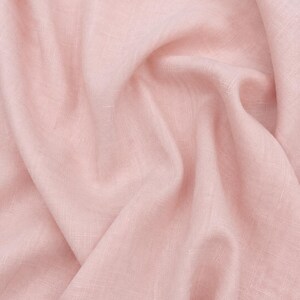 Op de afbeelding: Een stuk lichtroze stof met een zichtbare geweven textuur en zachte plooien. De tekst 05 Blush Magnolia is in het zwart gedrukt in het midden bovenaan de afbeelding. Het materiaal heeft een matte afwerking en een consistente lichtroze kleur.