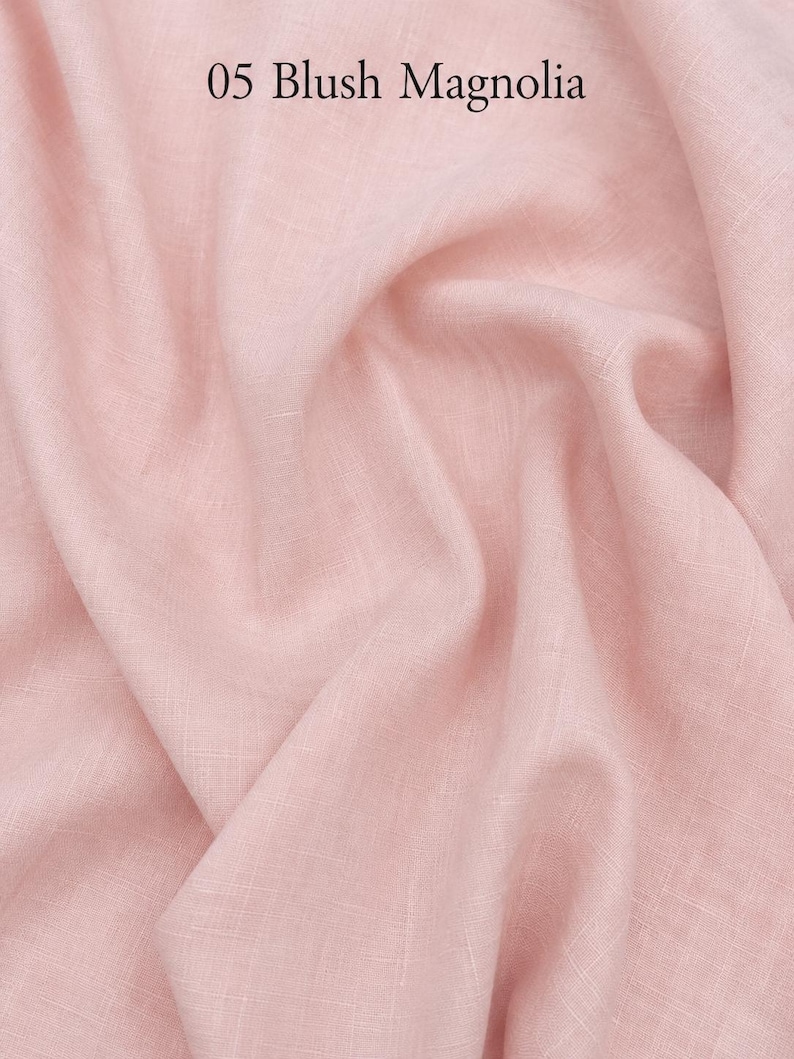 Op de afbeelding: Een stuk lichtroze stof met een zichtbare geweven textuur en zachte plooien. De tekst 05 Blush Magnolia is in het zwart gedrukt in het midden bovenaan de afbeelding. Het materiaal heeft een matte afwerking en een consistente lichtroze kleur.