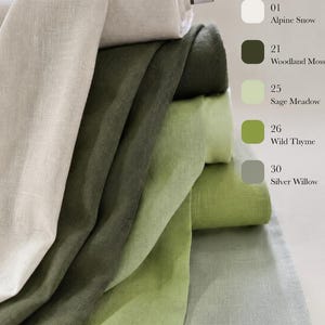 May include: A stack of five folded linen fabric bolts in shades of white, dark green, light green, olive green, and gray. The colors are labeled as 01 Alpine Snow, 21 Woodland Moss, 25 Sage Meadow, 26 Wild Thyme, and 30 Silver Willow on the right.
