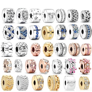 May include: A collection of thirty-five metal charm beads in various finishes including silver, gold, and rose gold tones. The beads feature diverse designs such as clear crystals, blue stones, pink enamel flowers, star patterns, and heart motifs.