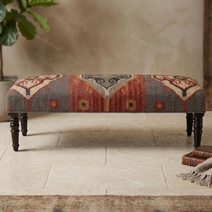 May include: A rectangular bench featuring a woven textile top with a geometric pattern in shades of charcoal gray, rust orange, and cream. The bench is supported by four dark brown, turned wooden legs with a classic spindle design.