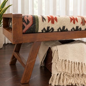 May include: A wooden bench featuring a rectangular seat upholstered in a woven fabric with a multi-colored geometric pattern in shades of red, green, and black on a cream background. The bench has angled wooden legs and a solid frame.