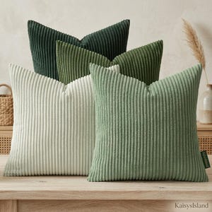 May include: A collection of four square throw pillows featuring a vertical corduroy texture. The pillows are arranged in a gradient of green shades, ranging from a deep forest green and olive green to a soft sage green and a light cream color.