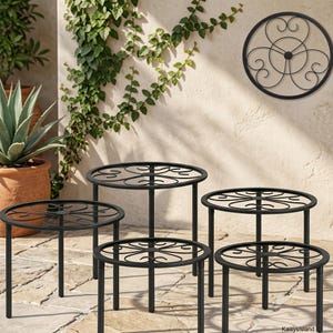 May include: A set of five black metal plant stands of varying heights, each featuring a circular top with a decorative scrollwork pattern. The stands have thin, straight legs and are arranged in a tiered formation for display purposes.