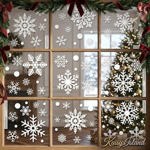 May include: A set of white snowflake window decals featuring various intricate geometric patterns and small circular dots. The stickers are applied to a multi-pane window frame decorated with green pine garlands and red bows.
