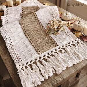 May include: A table runner featuring alternating vertical panels of white crocheted lace and natural tan woven fabric. The runner is finished with long, knotted white fringe at the ends. The text KaisysIsland is visible in the upper right corner.