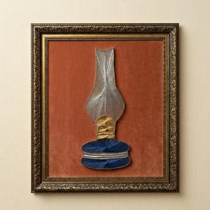 May include: A string art piece depicting a vintage oil lamp in a dark ornate frame. The lamp design is created with silver, gold, and navy blue threads against a burnt orange velvet background, showcasing a detailed silhouette of the lamp.