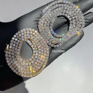 May include: Two circular tennis necklaces, one in gold and one in silver, featuring rows of clear, faceted stones that reflect light. The text FOREVERGEMS is printed in white between the two necklaces, which are displayed on a dark surface.