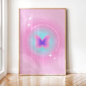 Puede incluir: Una lámina decorativa rectangular en un marco de madera clara con un fondo degradado en rosa y azul y una silueta de mariposa morada en el centro. El texto dice: SOY ABUNDANCIA Y TODO LO QUE PIDO EL UNIVERSO ME LO DA, decorado con cuatro estrellas blancas.
