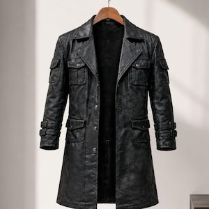 May include: A black long-length coat featuring a notched collar, a button-front closure, and a dark interior lining. The coat includes two chest pockets with flaps, two lower pockets with flaps, and adjustable buckle straps on each sleeve cuff.