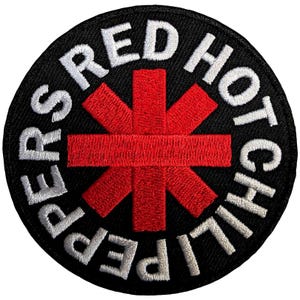 Peut inclure: Un écusson brodé circulaire avec un fond noir et un symbole rouge vif en forme d'astérisque au centre. Le texte blanc "RED HOT CHILI PEPPERS" est brodé en suivant une forme circulaire autour de l'élément graphique rouge central.