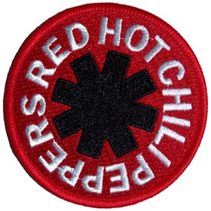 Peut inclure: Un écusson brodé circulaire présentant un fond rouge vif avec un emblème en forme d'étoile noire à huit branches au centre. Le texte blanc RED HOT CHILI PEPPERS est brodé en motif circulaire autour du motif central en étoile noire.