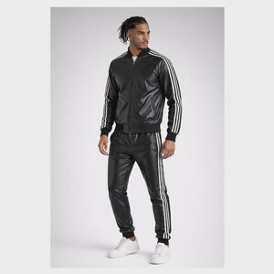 May include: A black faux leather tracksuit consisting of a zip-up jacket and matching trousers. Both pieces feature three white stripes running down the sleeves and legs. The jacket has a ribbed collar, cuffs, and hem, paired with white sneakers.
