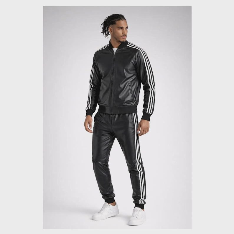 May include: A black faux leather tracksuit consisting of a zip-up jacket and matching trousers. Both pieces feature three white stripes running down the sleeves and legs. The jacket has a ribbed collar, cuffs, and hem, paired with white sneakers.