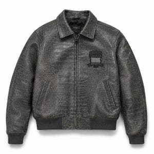 Op de afbeelding: Een antracietgrijze leren jas met een textuur van krokodillenleer, voorzien van een ritssluiting aan de voorzijde, een standaard kraag, geribbelde boorden en zoom, en een zwarte geborduurde patch op de linkerborst met een vlagmotief.