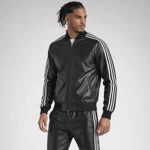 May include: A black faux leather track jacket featuring a full-length front zipper, a ribbed collar, and three white stripes running down the length of each sleeve. The jacket includes two zippered side pockets and ribbed cuffs at the wrists.