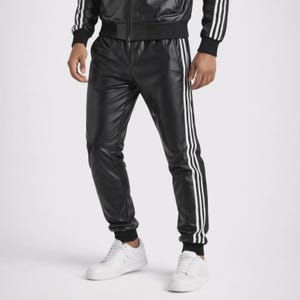 May include: Black faux leather track pants featuring three vertical white stripes running down the outer sides of each leg, paired with a matching black track jacket with white stripes on the sleeves and white sneakers.