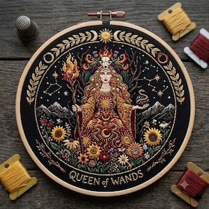 May include: A circular embroidery hoop featuring a detailed needlework design on black fabric. The central figure is a woman with long hair, wearing a crown with a skull, holding a flaming staff and a snake. Text reads QUEEN of WANDS.