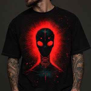 Puede incluir: Una camiseta negra de manga corta con un estampado gráfico de una cabeza alienígena oscura y estilizada rodeada por un aura roja brillante y vibrante con efectos de salpicaduras y un detalle de cuello acanalado en el centro del pecho.