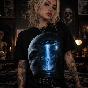 以下が含まれることがあります： 黒の半袖Tシャツで、エイリアンの頭部のシルエットが大きくプリントされています。頭部の中には暗い森の風景が描かれており、光り輝く青いUFOが中央に浮かぶ人物を照らしているデザインが特徴です。