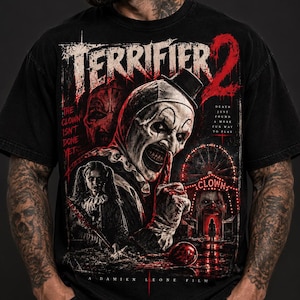 Może przedstawiać: Czarny t-shirt z krótkim rękawem z grafiką z filmu Terrifier 2. Wzór przedstawia postać klauna, diabelski młyn oraz tekst: Terrifier 2, The Clown Isn't Done Yet, Death Just Found A More Fun Way To Play.