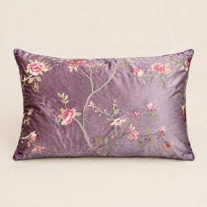 May include: A rectangular throw pillow in a muted purple velvet fabric. The surface features an embroidered pattern of delicate branches with pink and white flowers and green leaves, extending across the front of the pillow cover.