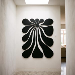 May include: A large, black, flat wall-mounted art piece featuring a central circular point from which multiple elongated, rounded, petal-like shapes radiate outward in a symmetrical, organic pattern against a plain, light-colored wall surface.