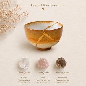 May include: A ceramic bowl with a gold-filled crack repair, featuring a gradient of amber to cream tones. Below are three raw stones labeled Clear Quartz, Rose Quartz, and Smoky Quartz, with text stating Includes 3 Story Stones above the bowl.