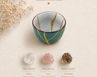 Puede incluir: Un cuenco de cerámica color verde azulado con grietas doradas, acompañado de tres piedras en bruto etiquetadas como Clear Quartz, Rose Quartz y Smoky Quartz. El texto incluye Includes 3 Story Stones, Clarity, Love y Grounding.