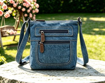 May include: A blue denim crossbody bag featuring a rectangular silhouette, two front zippered pockets with brown leather-like pull tabs, contrast stitching, and an adjustable shoulder strap. The bag has a structured design with a top zipper closure.