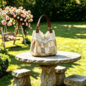 May include: A hobo-style handbag featuring a patchwork pattern of floral and checkered squares in shades of green, pink, and white. The bag is accented with a wide band of cream-colored lace at the top and includes brown leather handles with gold rings.