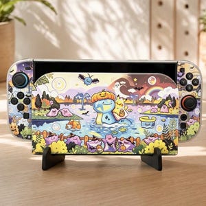 May include: A handheld gaming console featuring a colorful Halloween-themed skin with cartoon characters including a blue creature wearing a pumpkin, a yellow electric mouse, and several pink blobs in a landscape with a rainbow and bats.