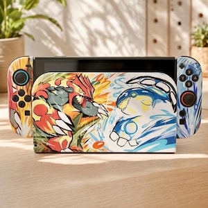 May include: A video game console dock and two controllers featuring a vibrant graphic illustration of a red, armored creature facing a blue, whale-like creature. The design incorporates dynamic splashes of orange, yellow, and blue colors.