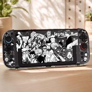 以下が含まれることがあります： Hunter x Hunterのアニメキャラクターのイラストが描かれた、白黒の保護スキン付きの携帯ゲーム機。デザインには、様々なマンガスタイルのキャラクター、クモのエンブレム、稲妻の模様が前面に施されています。