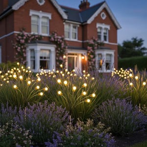 May include: Multiple solar garden lights featuring thin black stems topped with glowing warm white bulbs, arranged in a cluster among purple lavender plants. The lights are positioned in a garden bed in front of a brick house at twilight.