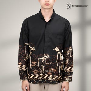 May include: A black long-sleeve button-down shirt featuring a tan and brown batik-style print of traditional shadow puppet figures along the lower torso and sleeves. The shirt includes a collar, a front pocket, and the text NFATELIERSHOP.