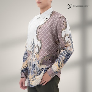 May include: A long-sleeved button-down shirt featuring a white collar and a split design. One side is solid white, while the other side displays a mauve and white lattice pattern with intricate dark blue and gold bird motifs. NFATELIERSHOP is printed.