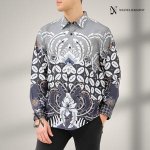 May include: A long-sleeve button-down shirt featuring a gray, black, and white batik-style pattern with intricate floral and geometric motifs. The shirt has a standard collar, a front button placket, and the text NFATELIERSHOP in the top right corner.