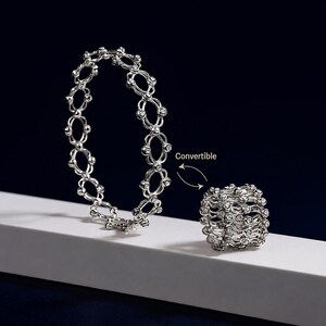 May include: A silver-toned metal bracelet composed of interconnected oval links set with small clear stones. The piece is labeled as Convertible, showing it can be adjusted into a multi-layered ring structure featuring the same linked design.