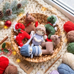 Może przedstawiać: Kolekcja szydełkowanych figurek amigurumi w plecionym koszyku, w tym czerwony renifer, zielony renifer, dwa brązowe renifery, mały aniołek w jasnoniebieskiej sukience i postać w niebieskim stroju, otoczone kłębkami włóczki i świątecznymi dekoracjami.