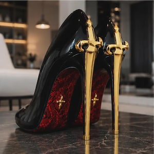 Könnte beinhalten: Ein Paar schwarze Lackleder-Pumps mit einem metallisch goldenen Stiletto-Absatz in Schwertform. Die Sohle des Schuhs ist mit einem roten Spitzenmuster bedeckt und in der Mitte des Fußgewölbes befindet sich ein kleines goldenes Kreuz-Emblem.