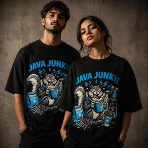 Könnte beinhalten: Ein schwarzes Kurzarm-T-Shirt mit einem Grafikdruck eines Eichhörnchens mit weit aufgerissenen Augen, das eine blaue Kaffeetasse hält. Der Text "JAVA JUNKIE" steht in Blau über dem Eichhörnchen, das von Kaffeebohnen, einer Tüte und einer Kaffeemaschine umgeben ist.