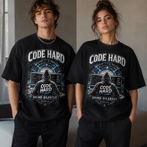 Puede incluir: Una camiseta negra de manga corta con un estampado gráfico de una figura encapuchada frente a un ordenador. El texto dice CODE HARD arriba y abajo, con GRIND SILENTLY y DevSync Labs debajo. El diseño incluye motivos de rayos azules y circuitos.